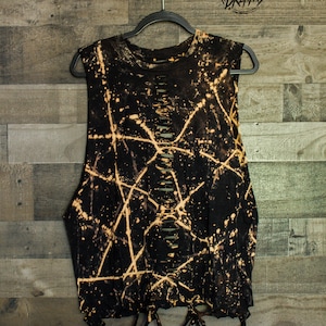 May include: Black sleeveless shirt with bleach splattered design and distressed detailing. The shirt has a round neckline and is hanging on a black hanger. The text "Shredded Dreams" is visible in the top right corner of the image.
