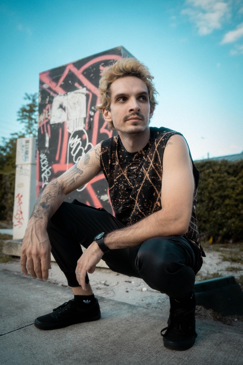 Peut inclure: Un haut sans manches noir avec un motif en losanges d&eacute;color&eacute; et des d&eacute;tails us&eacute;s, associ&eacute; &agrave; un pantalon de jogging noir et des baskets noires. Le haut pr&eacute;sente une encolure ronde et une coupe sans manches sur un tissu sombre avec des taches d&eacute;color&eacute;es.
