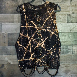 May include: A black sleeveless shirt featuring a bleached splatter pattern with thin, intersecting lines. The garment has a vertical row of horizontal slits running down the center of the chest and a frayed, cut-out hemline at the bottom edge.