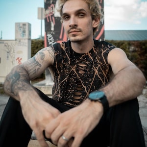 Peut inclure: Un haut sans manches noir avec un motif d&eacute;lav&eacute; &agrave; l'eau de Javel et une s&eacute;rie de d&eacute;coupes verticales sur le centre de la poitrine. Le v&ecirc;tement est associ&eacute; &agrave; un pantalon noir uni et une montre &agrave; cadran sombre avec un bracelet noir.