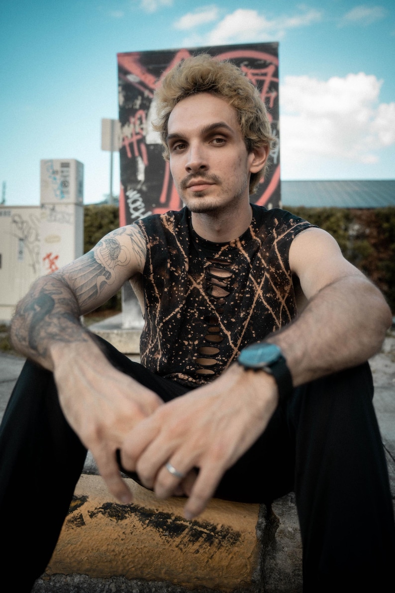 Peut inclure: Un haut sans manches noir avec un motif d&eacute;lav&eacute; &agrave; l'eau de Javel et une s&eacute;rie de d&eacute;coupes verticales sur le centre de la poitrine. Le v&ecirc;tement est associ&eacute; &agrave; un pantalon noir uni et une montre &agrave; cadran sombre avec un bracelet noir.
