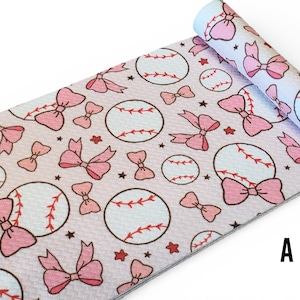 May include: A roll of fabric with a repeating pattern of baseballs, pink bows, and red stars on a light pink background. The baseballs have red stitching. The fabric is rolled up at the top, revealing the pattern on the back.