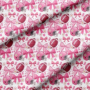 May include: A white fabric with a repeating pattern of pink football helmets, footballs, bows, daisies, and pink ribbons. The bows have a gingham pattern. The footballs and helmets are a darker shade of pink.