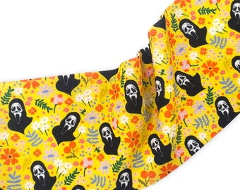 May include: Yellow fabric with a repeating pattern of black ghost faces and colorful flowers.