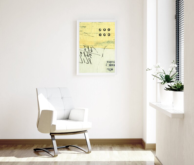 May include: A white chair with a black metal frame sits in a room with white walls and a framed abstract art print. The print features yellow and green colors with black text and circles. A window with white blinds is in the background.
