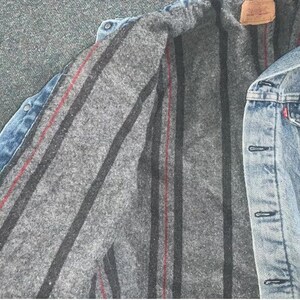 Pode incluir: Uma jaqueta de ganga azul com forro listrado cinza e vermelho. A jaqueta tem fecho de bot&otilde;es e v&aacute;rios bolsos.