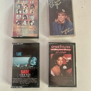 May include: Four cassette tapes with different artists and album titles. The tapes are all in black plastic cases with colorful artwork. The artists are The Bangles, Debbie Gibson, Sade, and Gloria Estefan. The album titles are "Different Light", "Electric Youth", "Diamond Life", and "Let It Loose".