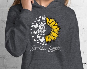 May include: A dark gray hooded sweatshirt with a sunflower and butterflies graphic. The sunflower is yellow and the butterflies are white. The text "Be the Light" is printed below the graphic.