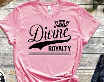 May include: Pink t-shirt with black text that reads "Divine Royalty" with a crown above the word "Divine".