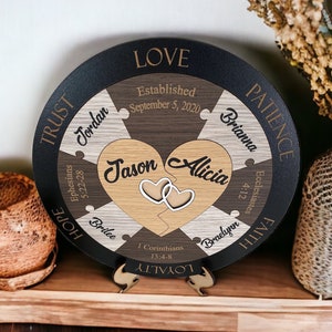 May include: A round wooden puzzle with a black background and a heart-shaped cutout in the center. The puzzle pieces are labeled with words like "Love", "Trust", "Hope", "Patience", "Faith", and "Loyalty". The heart-shaped cutout is filled with two smaller hearts, one labeled "Jason" and the other labeled "Alicia". The puzzle also includes the date "September 5, 2020" and the names "Jordan", "Brilee", "Brianna", and "Braelynn".