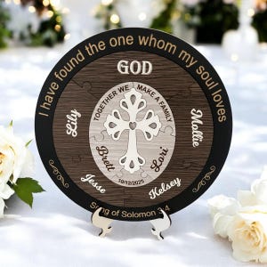 May include: A round wooden puzzle with a black border, featuring a cross design and the words "GOD" and "I have found the one whom my soul loves." Names and a date are also included. The puzzle is displayed on a white surface.