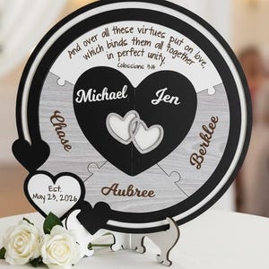 May include: A personalized wooden puzzle with a black and white design. The puzzle features names, hearts, and the text "And over all these virtues put on love, which binds them all together in perfect unity." A wedding or anniversary gift.