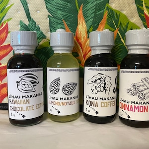 May include: Four small glass bottles with white labels and black caps. The labels have black and white illustrations of cocoa beans, almonds, coffee beans, and cinnamon sticks. The text on the labels reads "Lihau Makanas Hawaiian Chocolate Extract 1 oz", "Lihau Makanas Almond/Noyaux Extract 1 oz", "Lihau Makanas Kona Coffee 1 oz", and "Lihau Makanas Cinnamon Extract 1 oz".