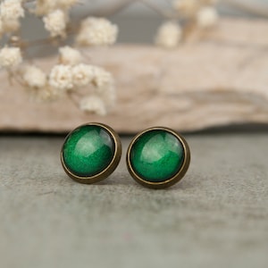 Könnte beinhalten: Ein Paar grüne Ohrstecker aus Bronze. Die Ohrstecker sind rund und haben eine metallische Oberfläche.