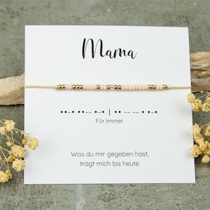 Könnte beinhalten: Ein Armband mit rosa und goldenen Perlen, präsentiert auf einer Karte mit dem Wort "Mama". Die Karte enthält auch den Text "Für Immer" und eine deutsche Nachricht. Trockenblumen und ein Stein befinden sich im Hintergrund.
