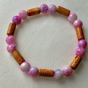 May include: A pink and white patterned bead bracelet with brown wooden beads.