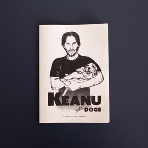May include: Monochrome print showing a man cradling a puppy, with the title "Keanu with Dogs" in bold lettering. The text "A film by John McCarvill" is also visible. The image is set against a dark blue background.