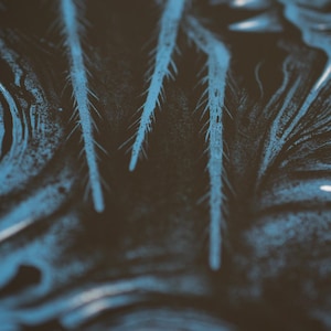 Puede incluir: Una superficie oscura con un patr&oacute;n abstracto de alto contraste, tonos negros profundos y remolinos fluidos de color azul vibrante. El dise&ntilde;o incluye estructuras afiladas, alargadas y similares a agujas que se extienden verticalmente.