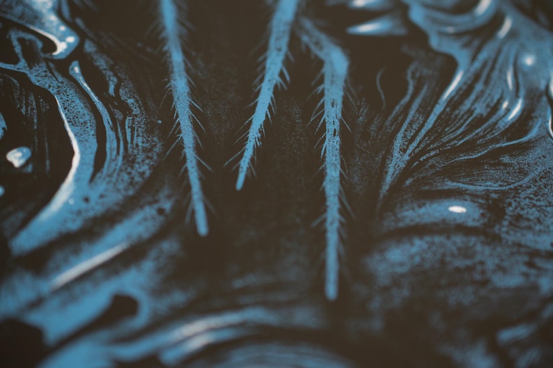 Puede incluir: Una superficie oscura con un patr&oacute;n abstracto de alto contraste, tonos negros profundos y remolinos fluidos de color azul vibrante. El dise&ntilde;o incluye estructuras afiladas, alargadas y similares a agujas que se extienden verticalmente.