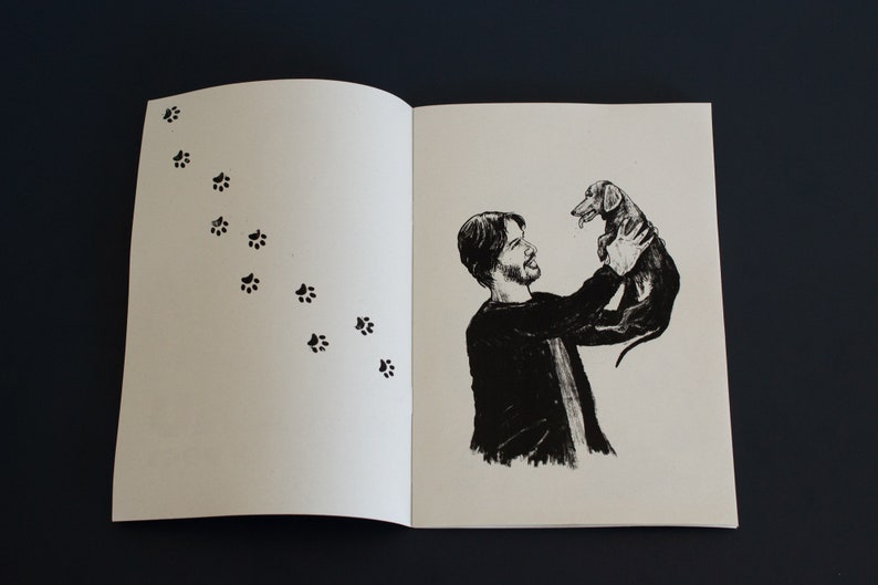 May include: Monochrome illustration of a person holding a dachshund dog. A trail of paw prints leads across the left page. The image is set against a dark background.