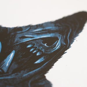 Puede incluir: Una ilustraci&oacute;n en serigraf&iacute;a que muestra una criatura oscura y estilizada con dientes afilados y una estructura facial similar a un cr&aacute;neo. La obra utiliza una paleta de colores de alto contraste en negro profundo y azul sobre fondo blanco.