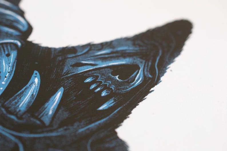 Puede incluir: Una ilustraci&oacute;n en serigraf&iacute;a que muestra una criatura oscura y estilizada con dientes afilados y una estructura facial similar a un cr&aacute;neo. La obra utiliza una paleta de colores de alto contraste en negro profundo y azul sobre fondo blanco.