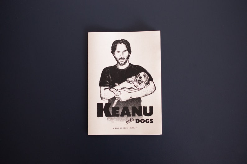 May include: Monochrome print showing a man cradling a puppy, with the title "Keanu with Dogs" in bold lettering. The text "A film by John McCarvill" is also visible. The image is set against a dark blue background.