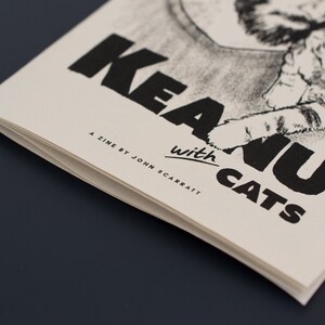 Pode incluir: Um fanzine intitulado "Keanu with Cats" com uma ilustra&ccedil;&atilde;o a preto e branco de um gato e texto. O fanzine &eacute; impresso em papel branco sujo com tinta preta. O nome do autor, John Scarratt, tamb&eacute;m est&aacute; impresso.