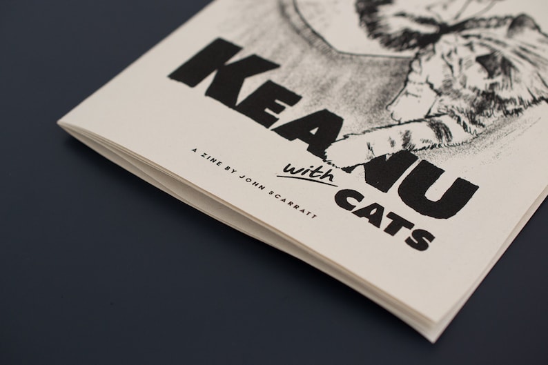 Pode incluir: Um fanzine intitulado "Keanu with Cats" com uma ilustra&ccedil;&atilde;o a preto e branco de um gato e texto. O fanzine &eacute; impresso em papel branco sujo com tinta preta. O nome do autor, John Scarratt, tamb&eacute;m est&aacute; impresso.