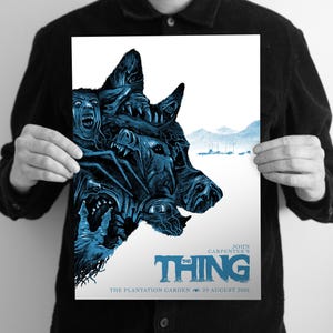 Puede incluir: Un p&oacute;ster rectangular con una ilustraci&oacute;n en azul y blanco de una criatura de m&uacute;ltiples caras. El texto dice John Carpenter's The Thing, The Plantation Garden, 25 August 2026. La obra representa una cabeza canina grande y distorsionada con ojos.