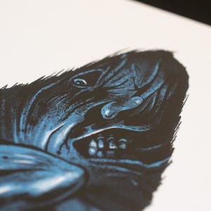 Puede incluir: Una impresi&oacute;n art&iacute;stica de alto contraste sobre papel blanco que presenta una ilustraci&oacute;n en azul oscuro y negro de una criatura con un rostro texturizado y expresivo. La figura muestra l&iacute;neas n&iacute;tidas y dentadas, una boca abierta con dientes.