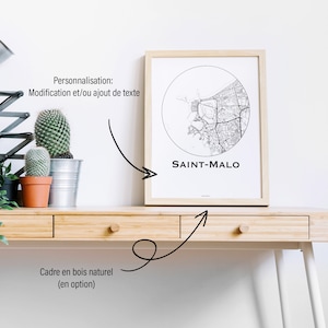 Peut inclure: Un cadre en bois clair avec une impression de carte en noir et blanc de Saint-Malo. La carte détaillée est encadrée dans un cercle. Le texte "SAINT-MALO" est visible. Le cadre est posé sur un bureau en bois clair.