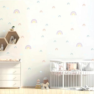 May include: A white wall with a nursery theme featuring multiple rainbow decals in pastel colours. The wall is decorated with a wooden hexagonal shelf and a white dresser. A white cot with a white mattress and a white blanket is in the foreground.