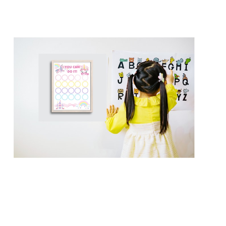 Peut inclure: Un enfant se tient devant un mur blanc avec deux affiches. L'affiche de gauche est un tableau color&eacute; avec des cercles &agrave; colorier et le texte "You Can Do It!" L'affiche de droite est un tableau de l'alphabet color&eacute; avec des animaux repr&eacute;sentant chaque lettre.