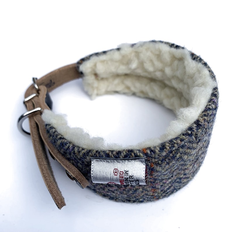 May include: A blue and brown tweed dog collar with a white fleece lining. The collar has a brown leather strap and a silver buckle. The collar has a label that says "The Tweed Collar Co."