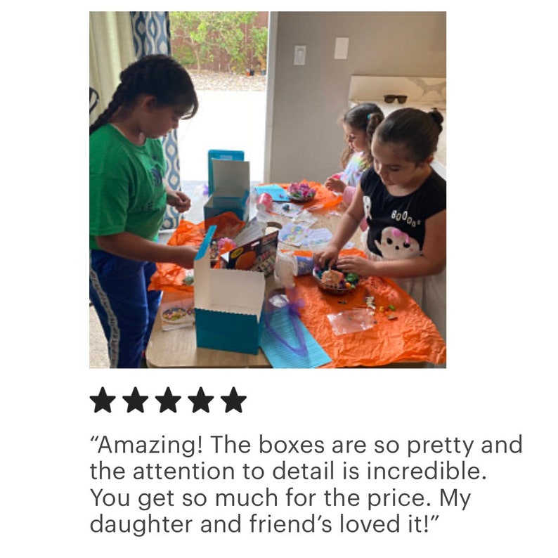 May include: Two children are working on a craft project. They are using colorful beads and other materials to create a fun and creative project. The project is in a blue box with a white lid. The box is on a table with an orange tablecloth. The children are smiling and having fun.