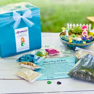 May include: A mermaid themed terrarium kit with a turquoise box, a clear glass bowl, and various bags of materials. The kit includes instructions for creating a mermaid garden. The text on the box reads "Mermaid Garden Kit".