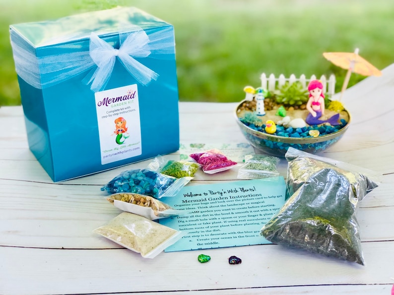 May include: A mermaid themed terrarium kit with a turquoise box, a clear glass bowl, and various bags of materials. The kit includes instructions for creating a mermaid garden. The text on the box reads "Mermaid Garden Kit".