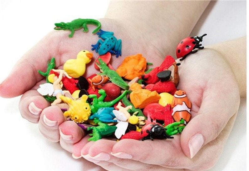 Pode incluir: Uma cole&ccedil;&atilde;o de figuras de animais de pl&aacute;stico coloridas, incluindo uma joaninha, um crocodilo, um sapo, um peixe, uma borboleta e alguns outros insetos. As figuras s&atilde;o todas pequenas e est&atilde;o sendo seguradas na m&atilde;o de uma pessoa.