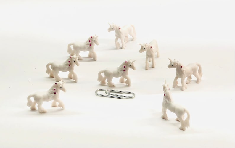 Pode incluir: Um grupo de oito figuras de unic&oacute;rnio brancas com detalhes rosa. Os unic&oacute;rnios est&atilde;o dispostos em c&iacute;rculo sobre um fundo branco.