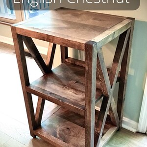 Pu&ograve; includere: Un'unit&agrave; a scaffale in legno con una finitura rustica. Lo scaffale ha tre ripiani e un design a forma di X sui lati. Lo scaffale &egrave; realizzato in legno marrone scuro con venature del legno naturali.