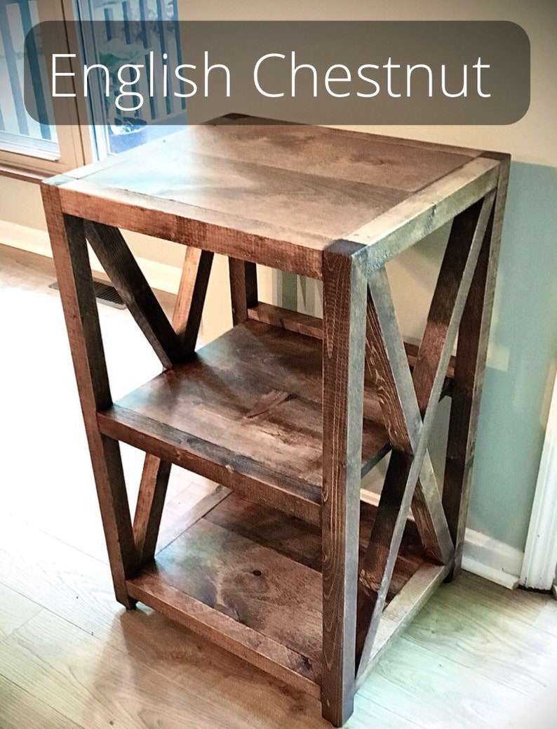 Pu&ograve; includere: Un'unit&agrave; a scaffale in legno con una finitura rustica. Lo scaffale ha tre ripiani e un design a forma di X sui lati. Lo scaffale &egrave; realizzato in legno marrone scuro con venature del legno naturali.