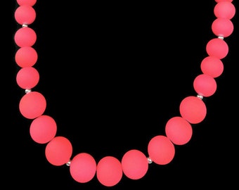 May include: A pink beaded necklace with silver accents. The beads are large and round, and the necklace is made of a soft, flexible material.