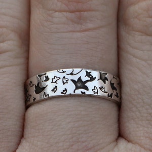 May include: A silver band ring with a repeating pattern of small birds and stars.