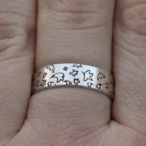 May include: A silver band ring with a repeating pattern of stars and crescent moons.