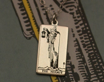 May include: A silver necklace with a rectangular pendant featuring a black and white illustration of The Hermit tarot card. The pendant has the text "THE HERMIT" printed on the bottom.