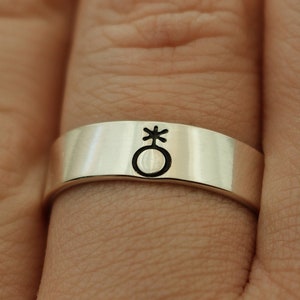 May include: A silver band ring with a black engraved symbol of a circle with a cross on top.