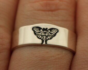 May include: A silver ring with a black butterfly design engraved on the band.