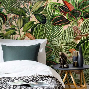 May include: A white bed with a black and white patterned blanket and a green pillow. The bed is in front of a wall with a tropical leaf wallpaper. A small wooden side table with a black top holds a small statue and two gold candle holders.