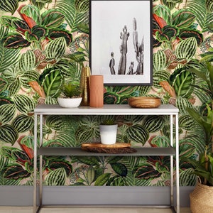 May include: A silver metal console table with two shelves. The table is in front of a wall with a tropical wallpaper featuring green and red leaves. There is a potted plant on the top shelf, a bowl of plants on the bottom shelf, and a framed print of cacti on the wall.